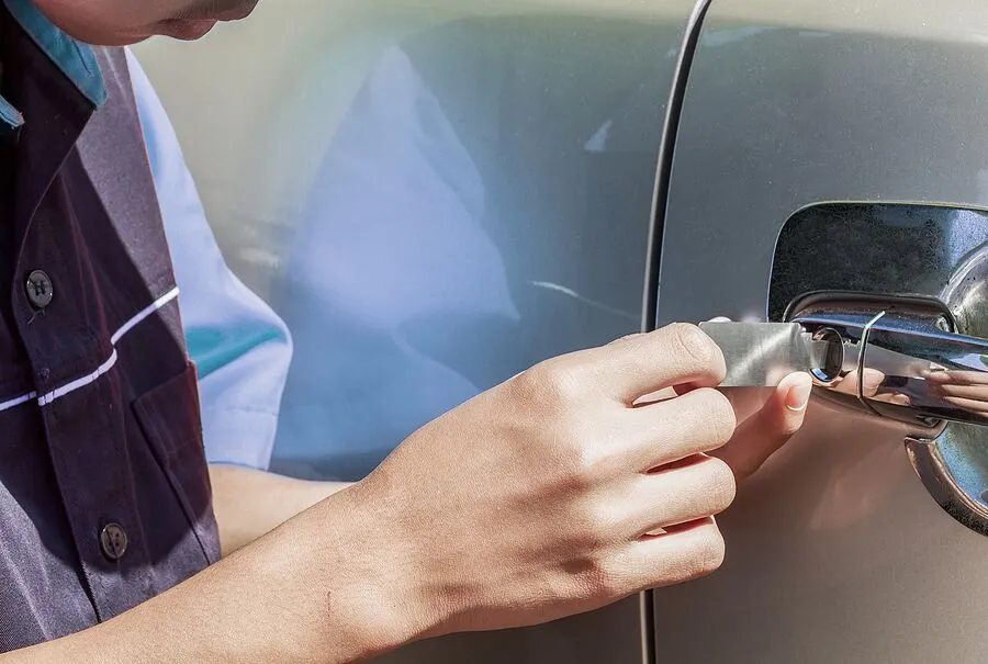 man inserting tools to open up door of automobile